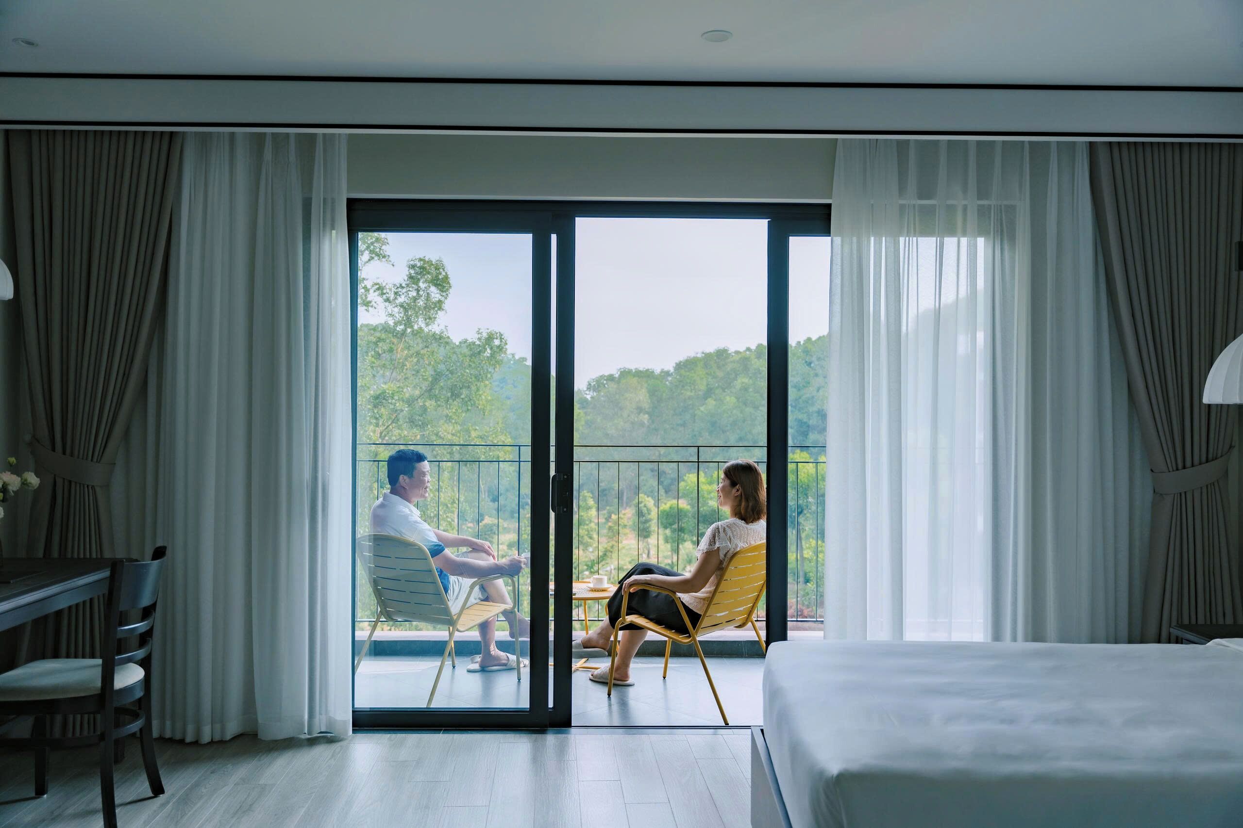 A hotel room with a balcony, a bed, a dining table, and chairs.