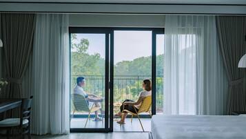 A hotel room with a balcony, a bed, a dining table, and chairs.