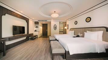 A hotel room with a large bed, a TV, a desk, and a bench.