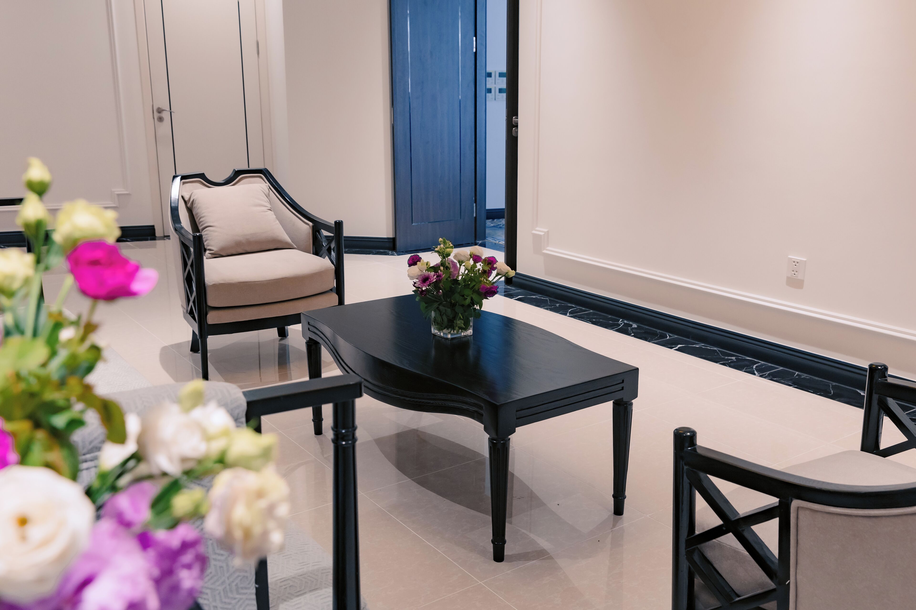 A dining area with a black table, beige chairs, and a vase of flowers.