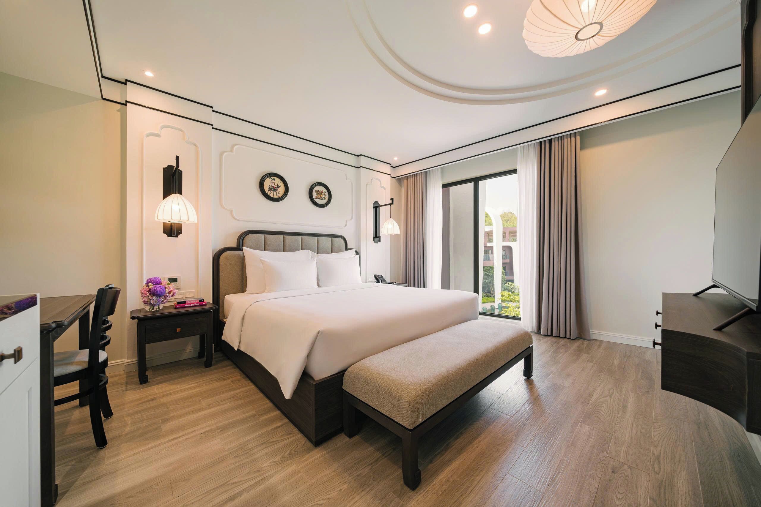 A modern hotel room with a large bed, bedside tables, a desk, and a TV.