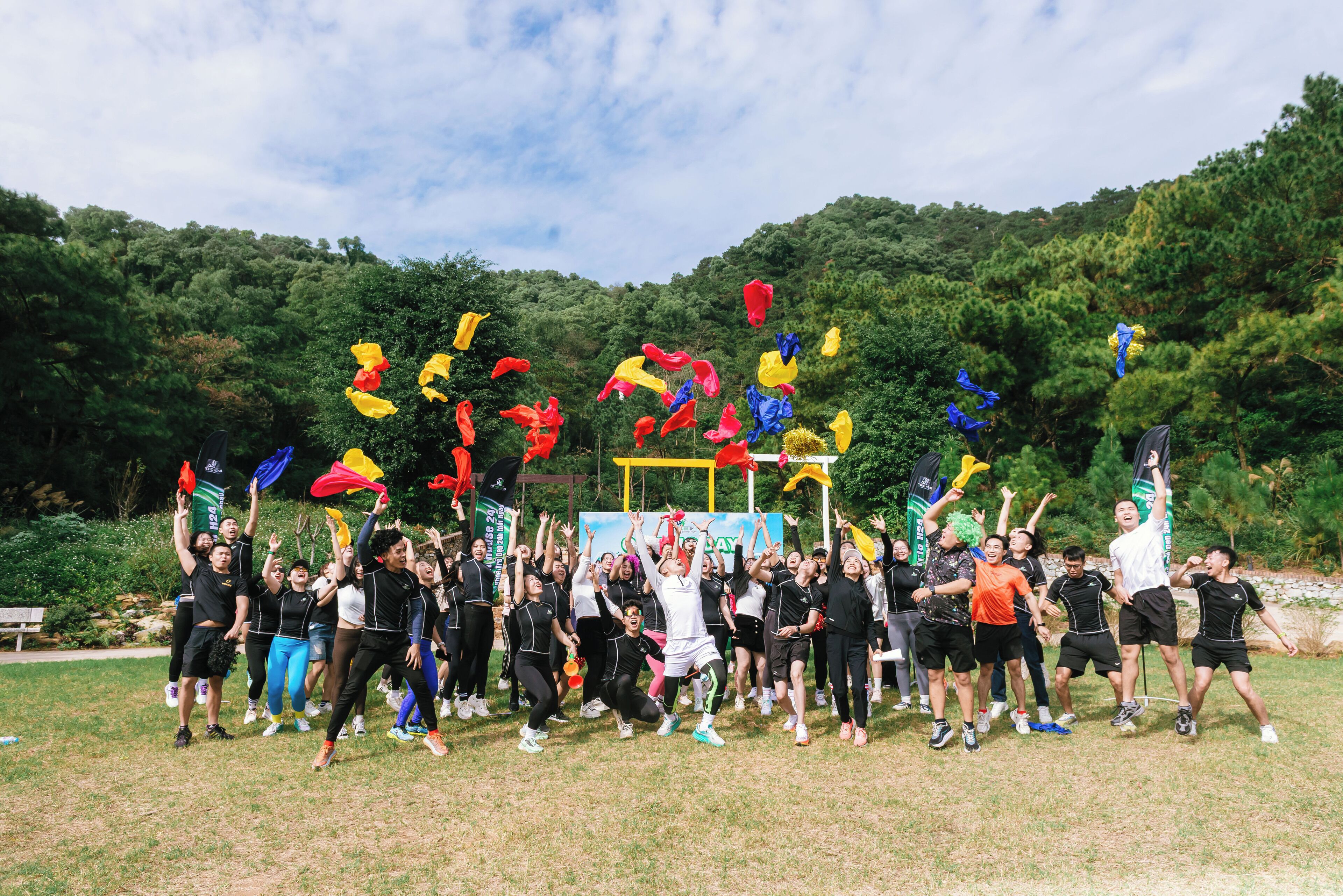 A group of people outdoors, possibly at a festival or event, with trees and a clear sky in the background.