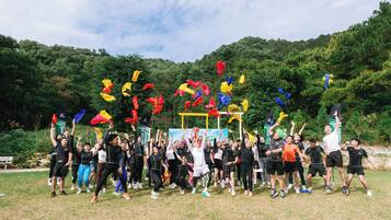 A group of people outdoors, possibly at a festival or event, with trees and a clear sky in the background.