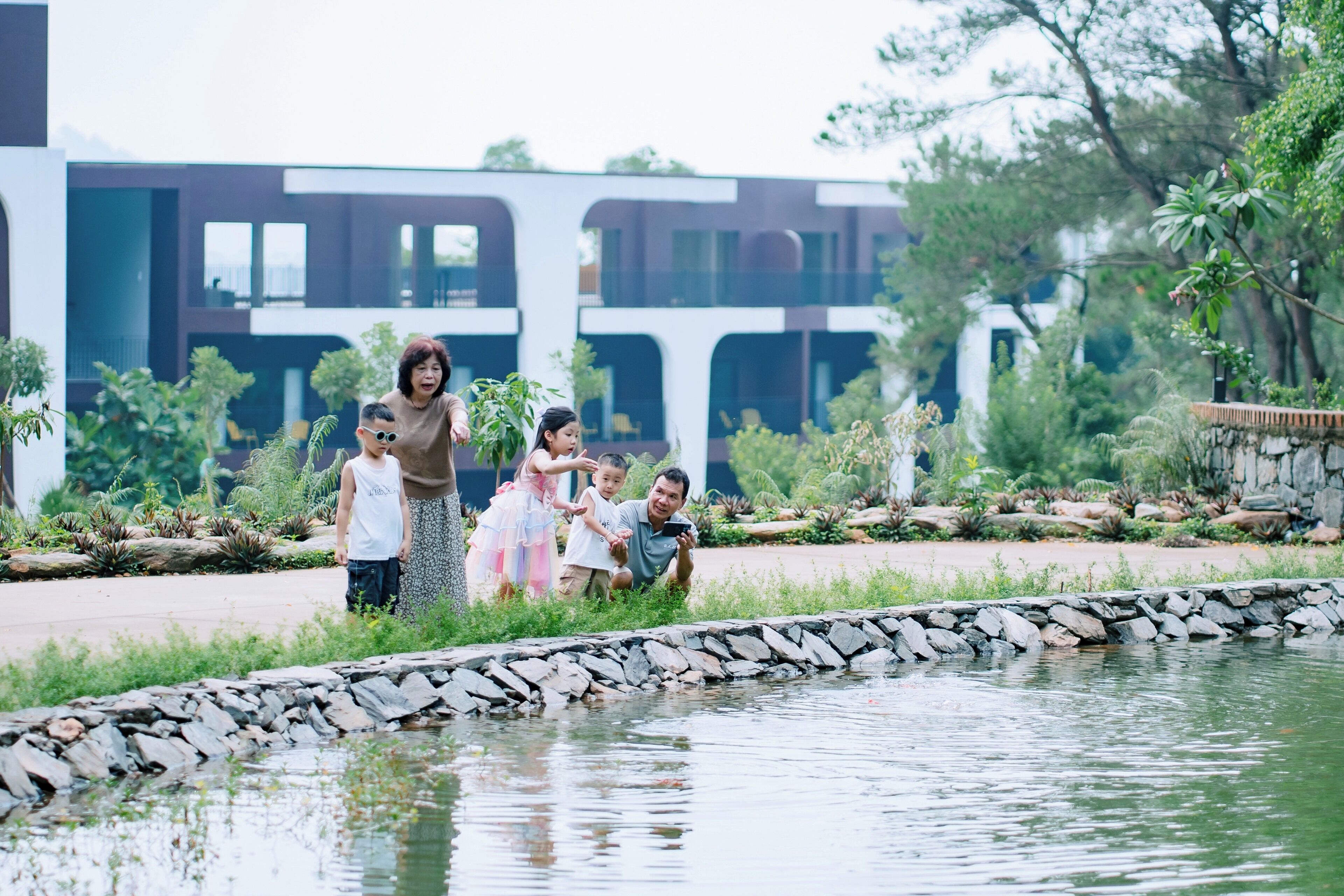 A group of people near a pond with a modern building in the background.