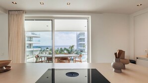 A modern kitchen with a large island, a view of a pool and buildings, and a dining area with wooden furniture. - Beachfront 2BR LUX Condo ONE Mambo 21 by Bocobay (Willemstad)