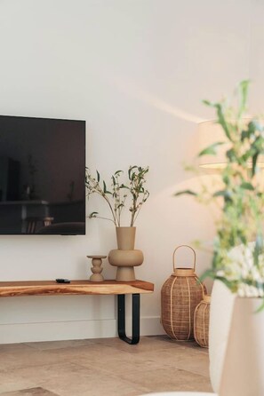 A modern living room with a flat-screen TV mounted on the wall, a wooden bench, and a potted plant.