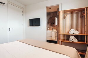 A bedroom with a bed, a TV, a wardrobe, and a bathroom with a mirror and towel rack.