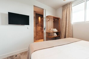 Et hotelværelse med en seng, et fjernsyn ophængt på væggen, et klædeskab med håndklæder og et vindue med gardiner.
