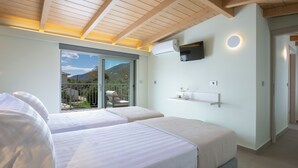 A bedroom with two beds, a TV mounted on the wall, and a balcony with a view of the mountains.