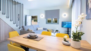 A modern living room with a wooden dining table, yellow chairs, a grey sofa, and a TV on the wall.