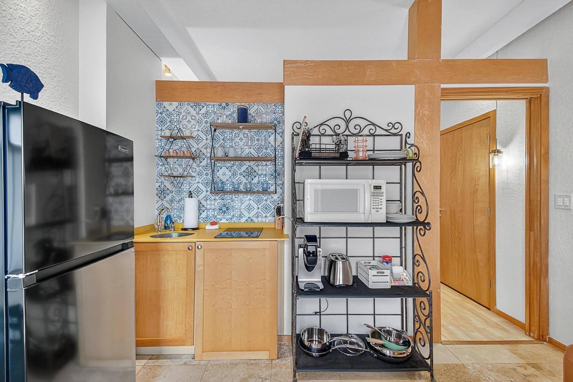 A compact kitchen with a microwave, coffee maker, and shelves for utensils.