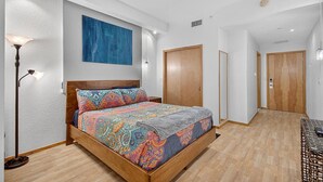 A bedroom with a wooden bed, a colorful patterned bedspread, a blue painting on the wall, and a floor lamp. - Market View Condo | European Village | Minutes to Beach & Restaurants (Palm Coast)