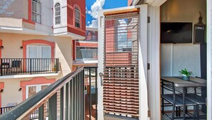 A balcony with a table and chairs, a potted plant, and a view of adjacent buildings. - Market View Condo | European Village | Minutes to Beach & Restaurants (Palm Coast)