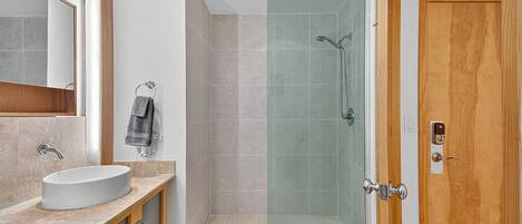 A modern bathroom with a glass-enclosed shower, a wooden vanity with a sink, and a mirror.