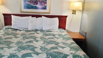 A neatly made bed with a floral bedspread, a framed picture on the wall, and a bedside lamp.