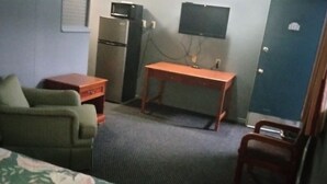 Habitació d'hotel amb llit, escriptori, cadira, televisió, nevera i porta.