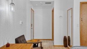 Een kamer met een houten eettafel, stoelen, een glazen hanglamp, een spiegel en twee houten deuren.
