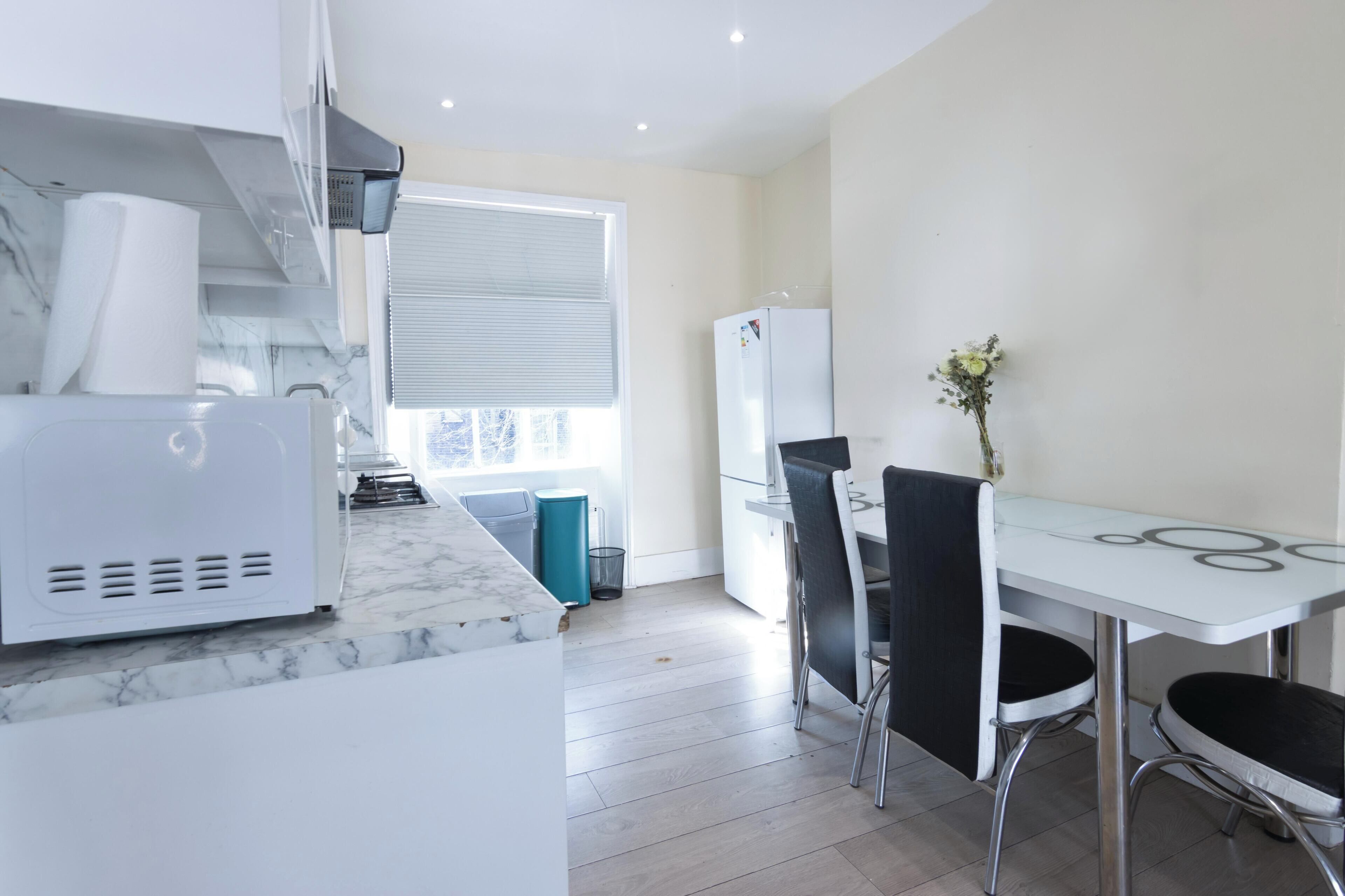 A modern kitchen with a marble countertop, a built-in oven, and a dining area with a glass table and black chairs.