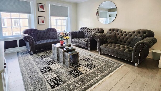 A living room with three dark sofas, a coffee table, and a patterned rug. - 2-bed Gucci Flat - Sleeps 6 & Close to Harrods (London)