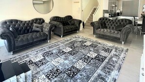 A living room with three dark, tufted sofas, a large patterned rug, and a mirror on the wall. - 2-bed Gucci Flat - Sleeps 6 & Close to Harrods (London)