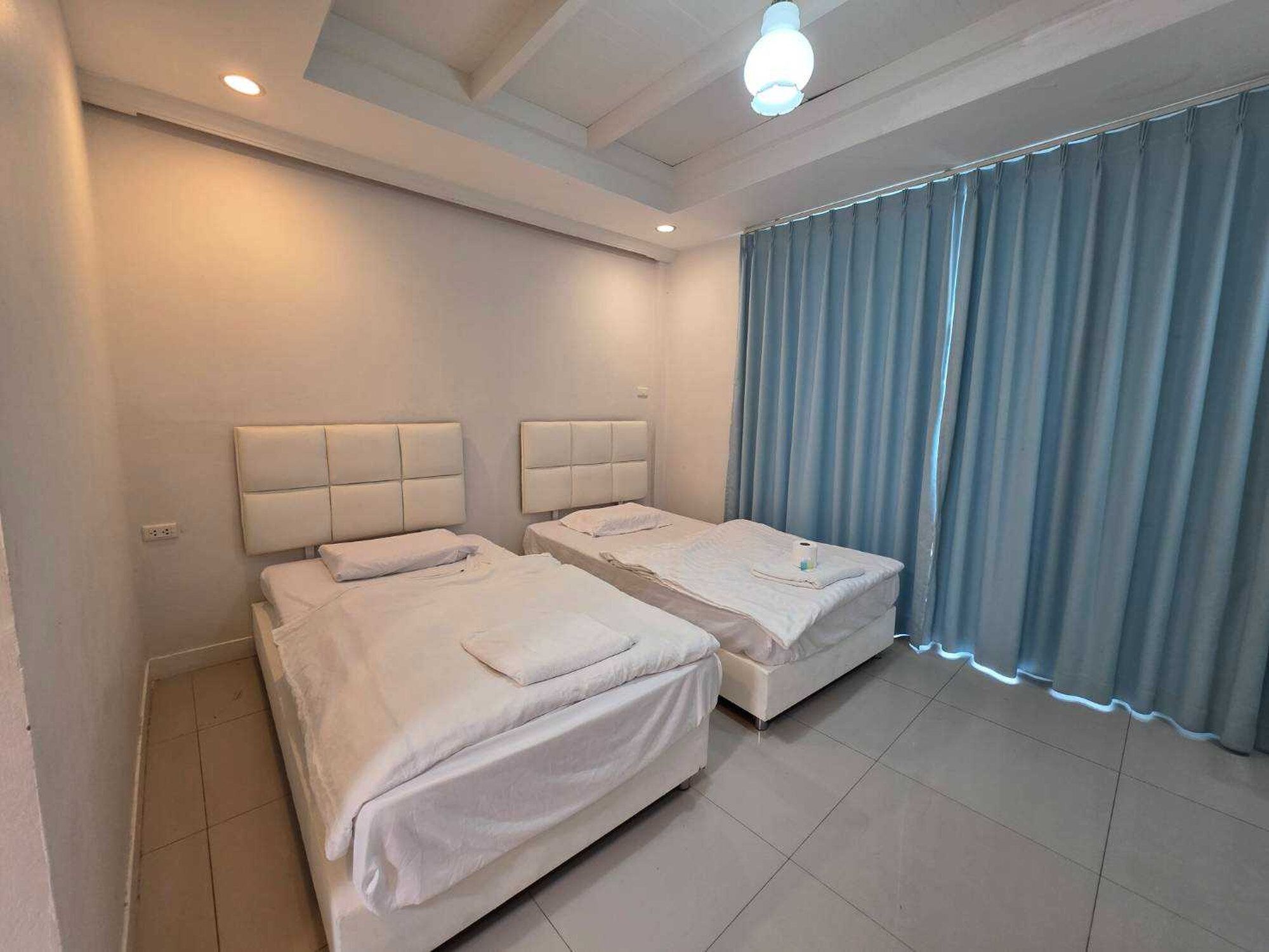 A hotel room with two beds, a large window with curtains, and a ceiling light.