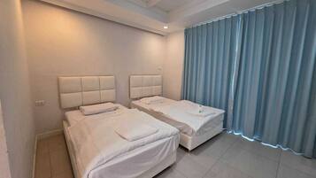 A hotel room with two beds, a large window with curtains, and a ceiling light.