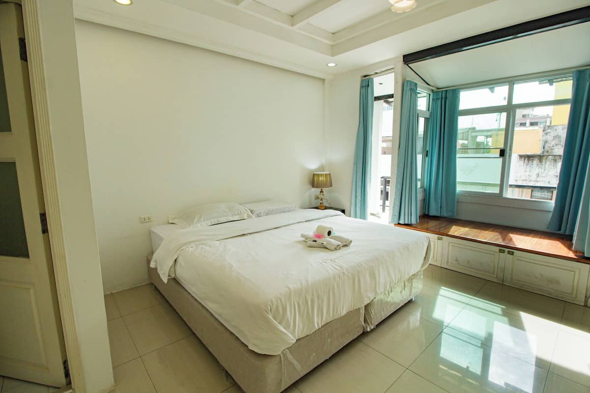 A bedroom with a large bed, a window with curtains, and a nightstand with a lamp.