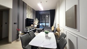 A modern dining area with a marble table, grey upholstered chairs, a black sofa, and a TV mounted on the wall. - 16th floor wonderland- 2 Bedroom (Dubai)
