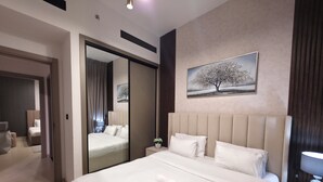 A modern hotel room with a large bed, a bedside table with a lamp, a painting of a tree, and a mirror reflecting the room. - 16th floor wonderland- 2 Bedroom (Dubai)
