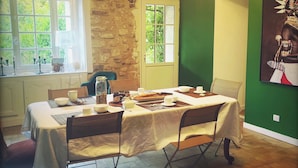A dining area with a table set for breakfast, a stone wall, a green wall, and a window with a view of greenery.