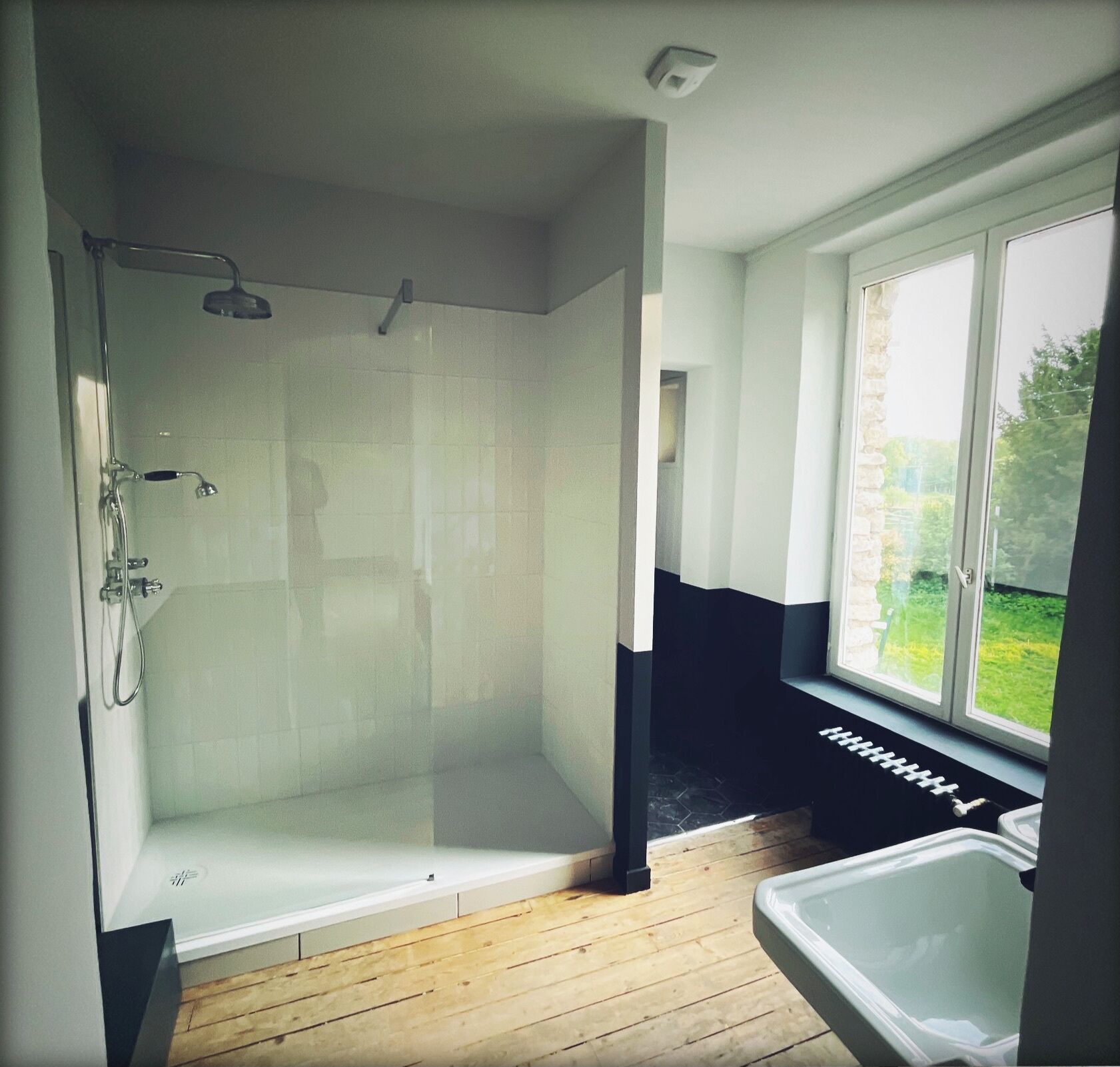 A modern bathroom with a glass shower enclosure, a bathtub, and a window providing a view of the outdoors.