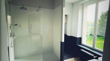 Een moderne badkamer met een glazen douchecabine, een badkuip en een raam met uitzicht op de omgeving.