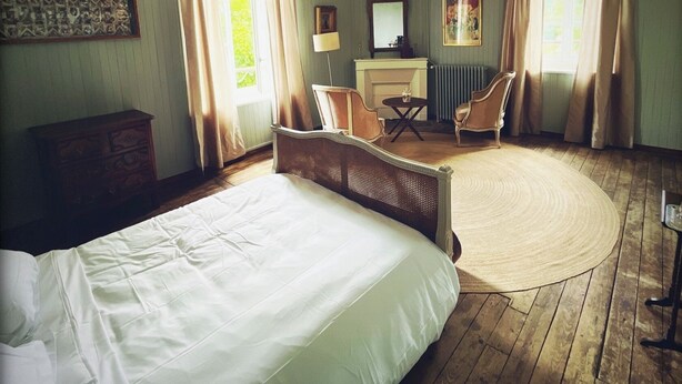 A bedroom with a large bed, a round rug, a desk, a chair, and a fireplace.