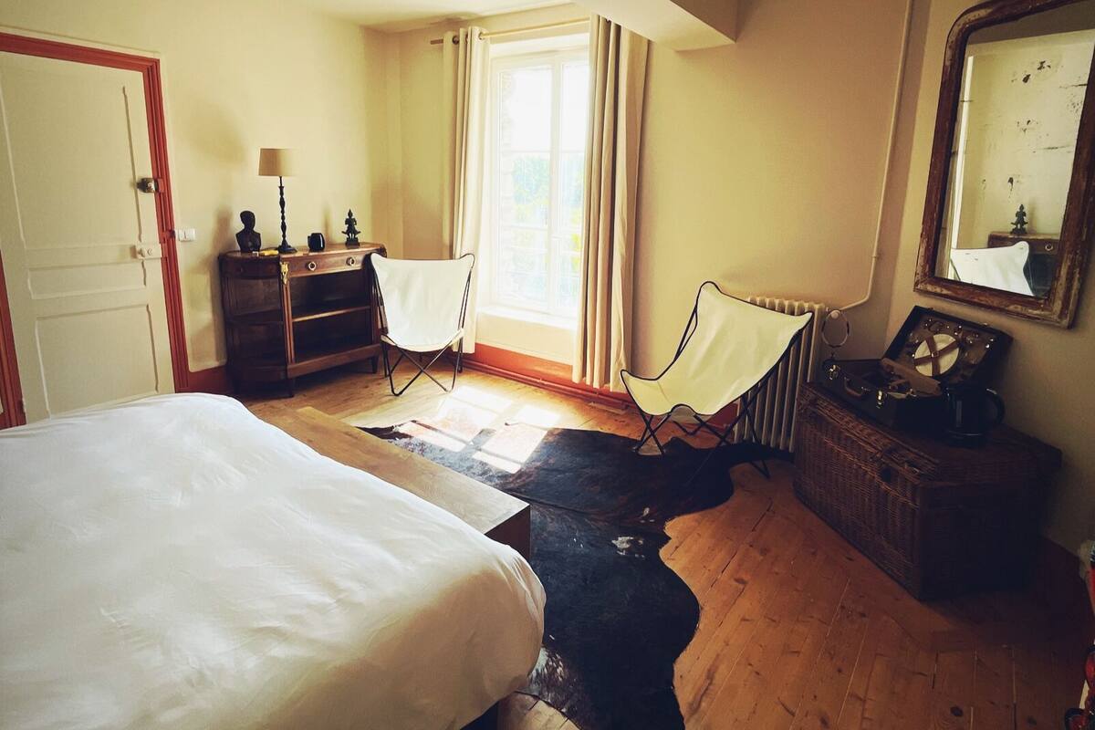 Une chambre à coucher avec un grand lit, une chaise, une commode, un radiateur et un miroir au mur.