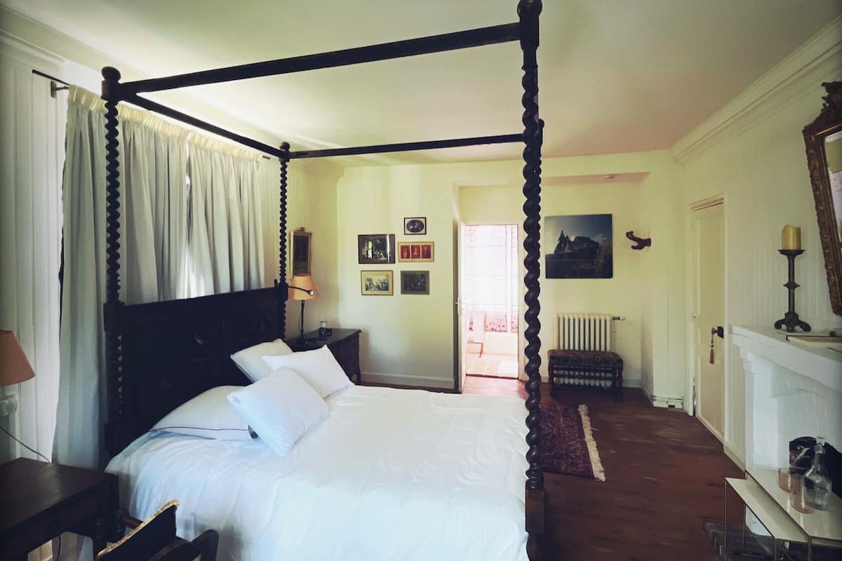 Un lit à baldaquin avec du linge de lit blanc, une table de chevet en bois, une lampe et un miroir au mur.