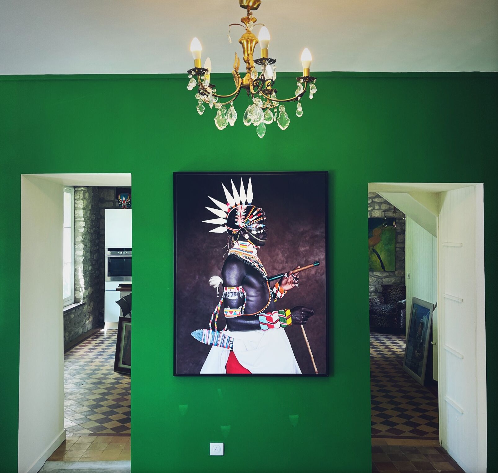 A hallway with green walls, a chandelier, and a framed artwork of a person with a spear.