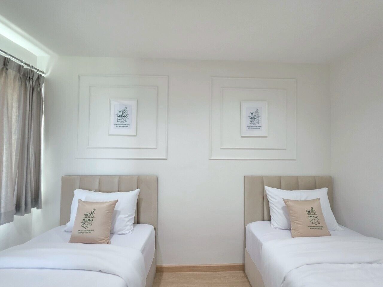 Habitación de hotel con dos camas individuales, cada una con cabecero color beige y ropa de cama blanca. Encima de cada cama hay cuadros enmarcados en la pared.
