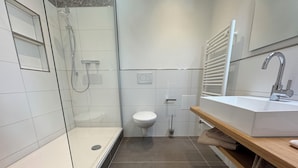 A modern bathroom with a glass shower enclosure, a white toilet, and a vanity with a sink and towel rack. - Vacation apartment Cochem Mosel Pinnerbergstube (Cochem)