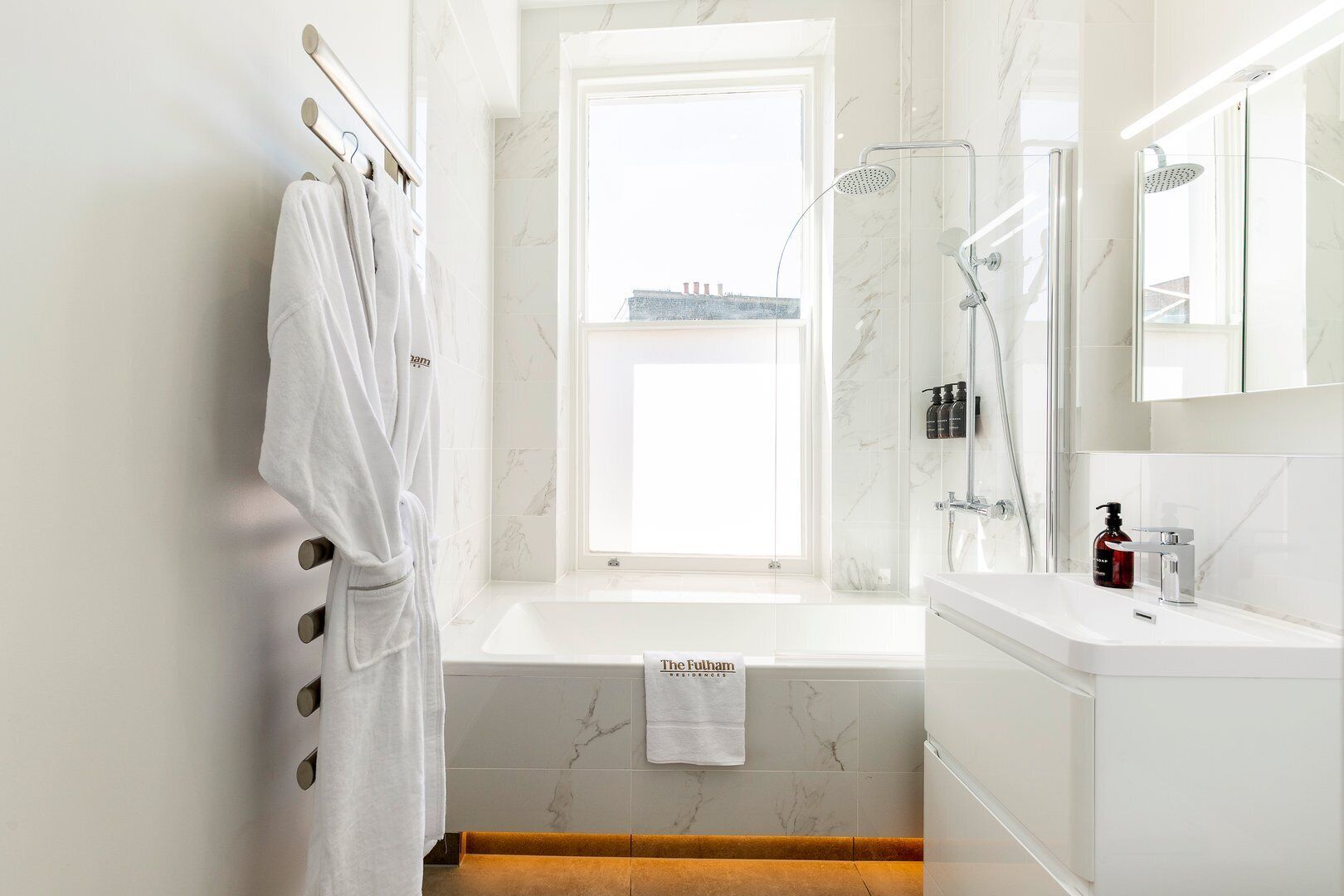 Un baño moderno con bañera, ducha y tocador con espejo. Hay una toalla colgada en la pared y una ventana que proporciona luz natural.