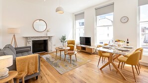 Een moderne woonkamer met een open haard, bank, televisie en een eetgedeelte met stoelen en een tafel.