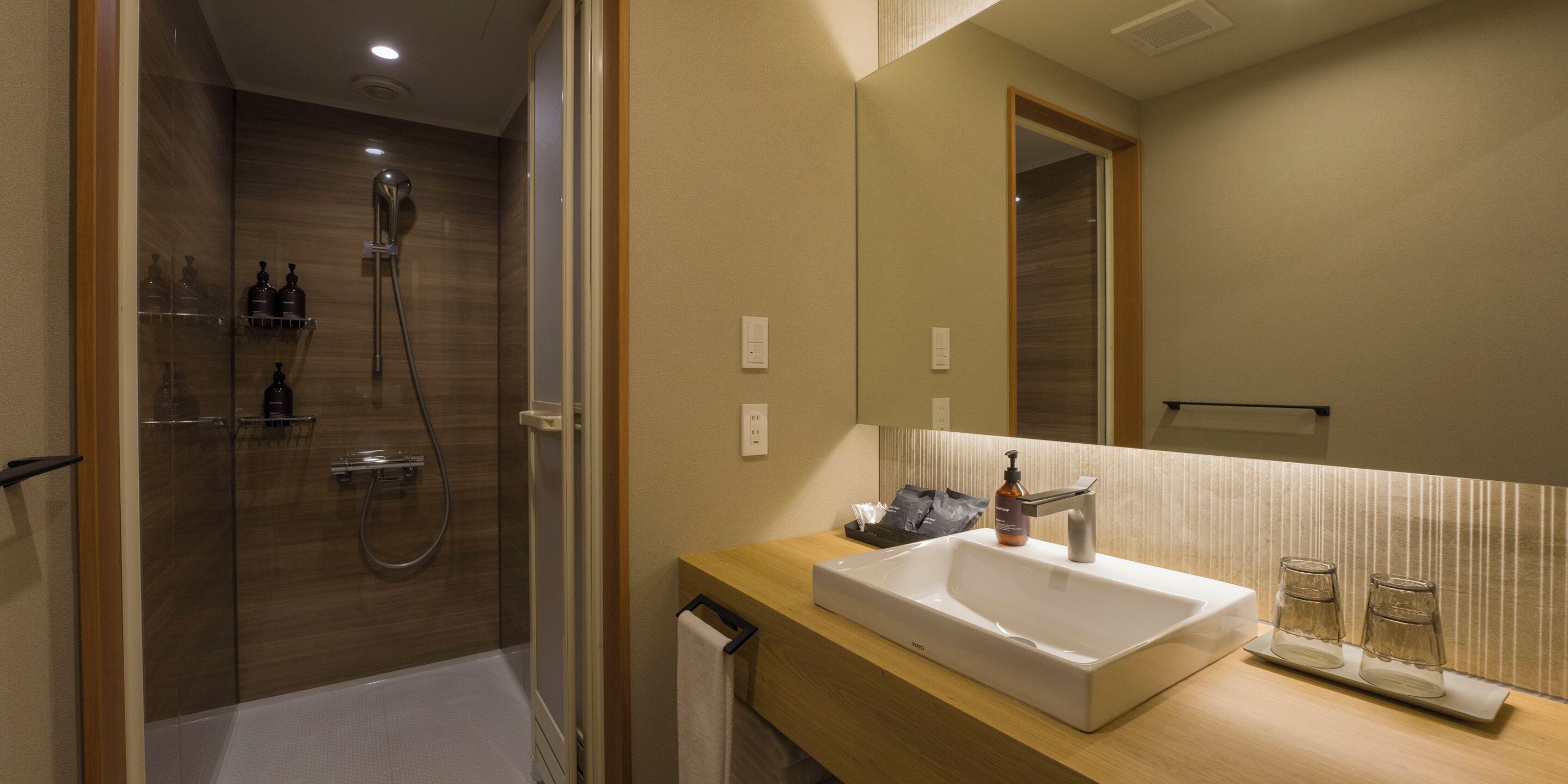 A modern bathroom with a walk-in shower, a large mirror, and a sink with a soap dispenser.
