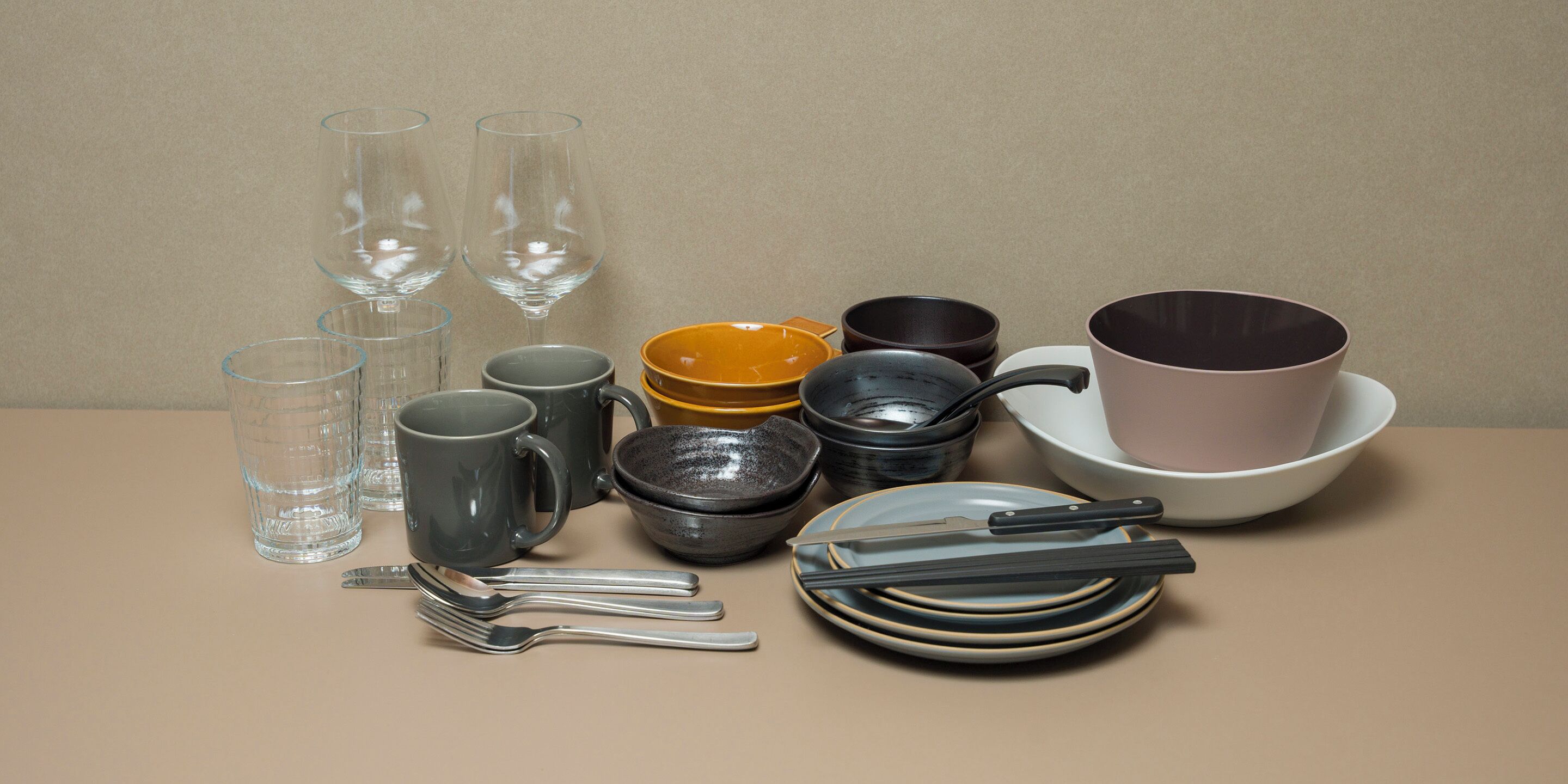 A table with various glassware, including multiple wine glasses, a mug, bowls, and plates, along with chopsticks and a knife.