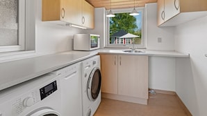 Une cuisine moderne avec des meubles en bois, un lave-linge encastré, un four à micro-ondes et une fenêtre donnant sur une maison.