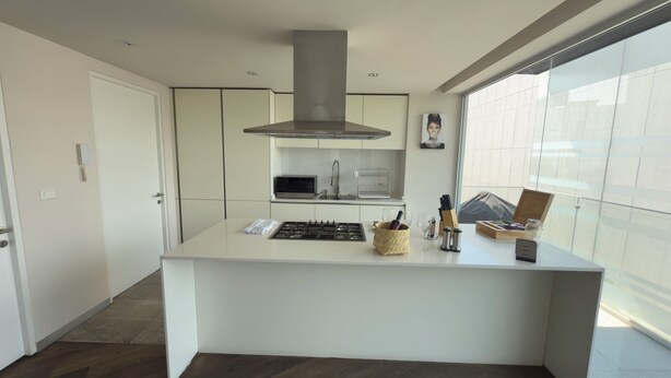 Cocina moderna con una isla central, electrodomésticos de acero inoxidable y un amplio ventanal que proporciona luz natural.