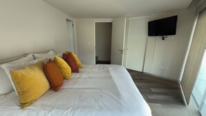 Un dormitorio con una cama grande, un televisor de pantalla plana montado en la pared y una puerta que da a otra habitación.