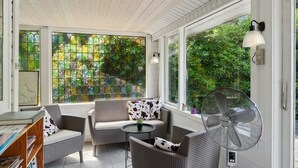 A sunlit room with wicker furniture, a fan, and large windows with green foliage outside. - "Rieke" -  from the sea by Interhome (Rørvig)
