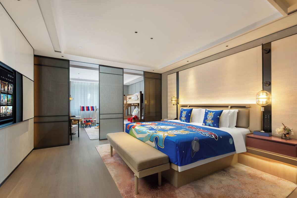 A modern hotel room with a large bed, a bench, a TV, and a desk.