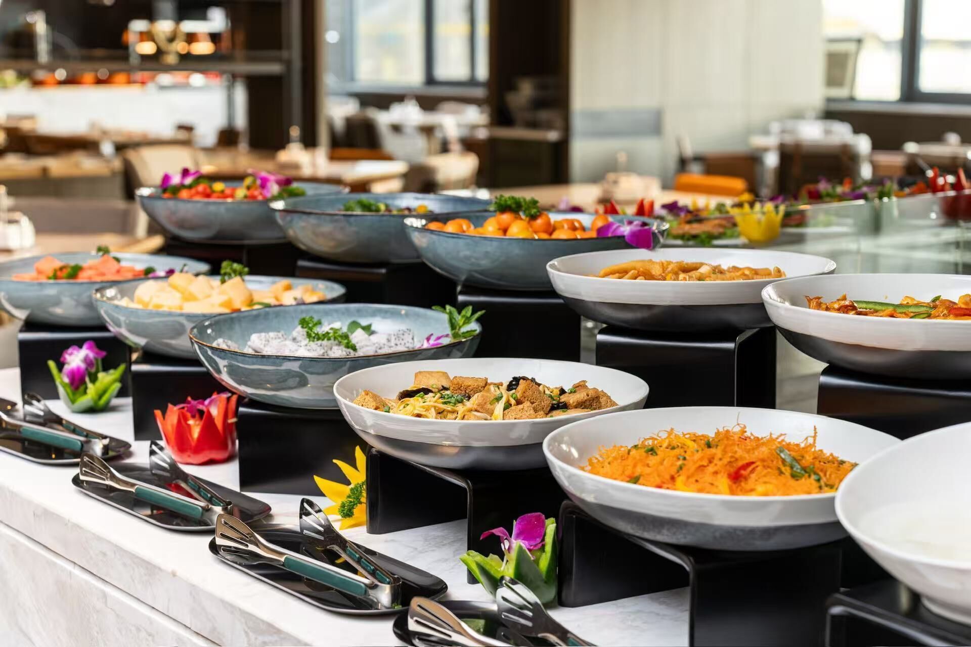 Ein Buffet mit verschiedenen Speisen, darunter Salate, Früchte und Gemüse, präsentiert auf schwarzen Ständern.