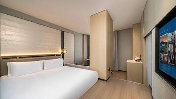 Habitación de hotel moderna con una cama grande, una mesita de noche, un espejo y un televisor de pared mostrando carteles de películas.
