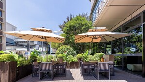 Un espace extérieur aménagé en terrasse, avec des tables et des chaises en bois, de grands parasols et des plantes en pot.